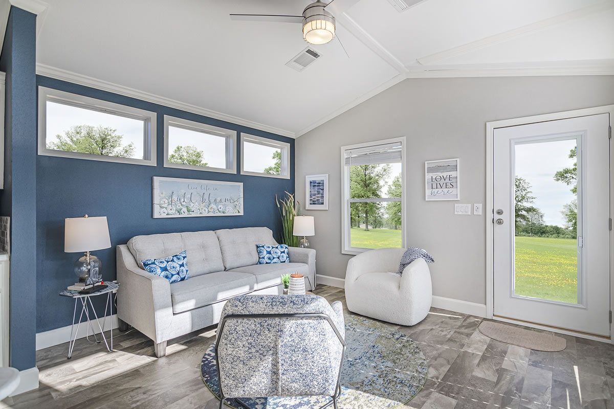 Bright living room with blue accent wall, gray sofa, and cozy chair. Large windows and door offer views of a green lawn; minimalistic decor adds calm ambiance.