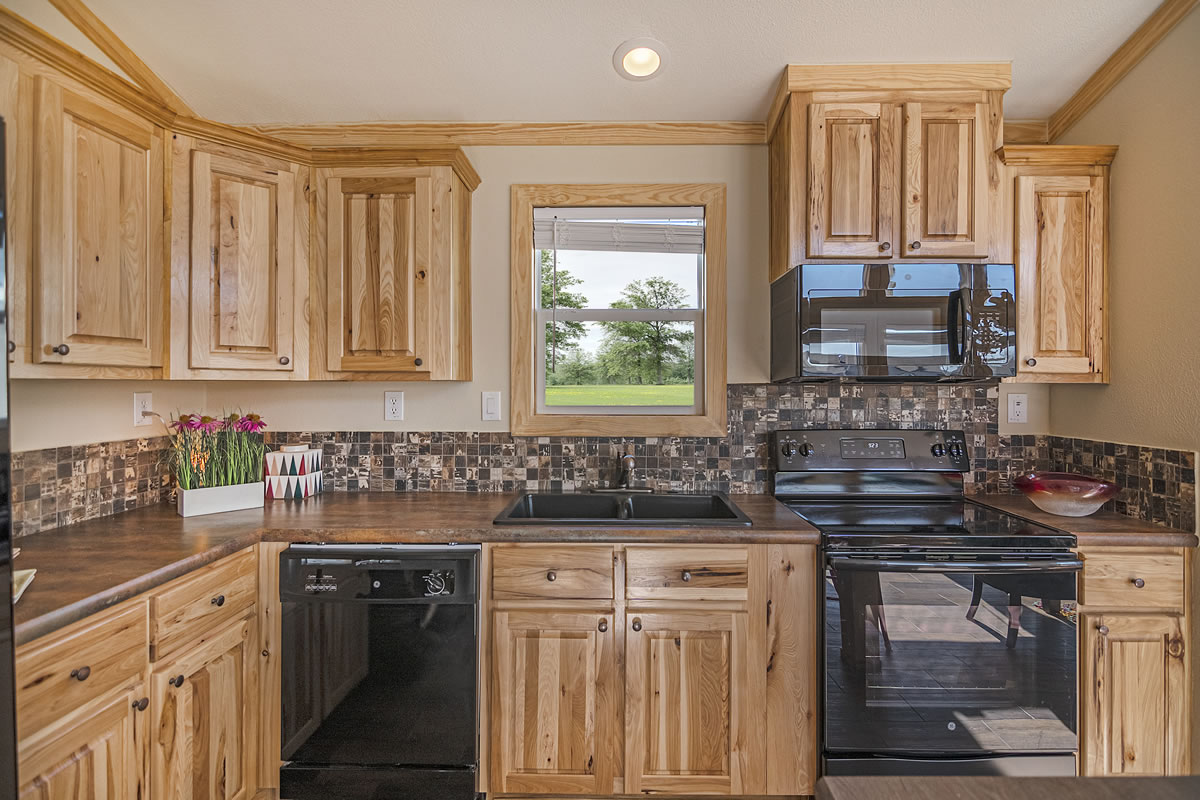 Cozy kitchen with wooden cabinets, black appliances, and a mosaic tile backsplash. A window overlooks greenery, adding a fresh, inviting feel.