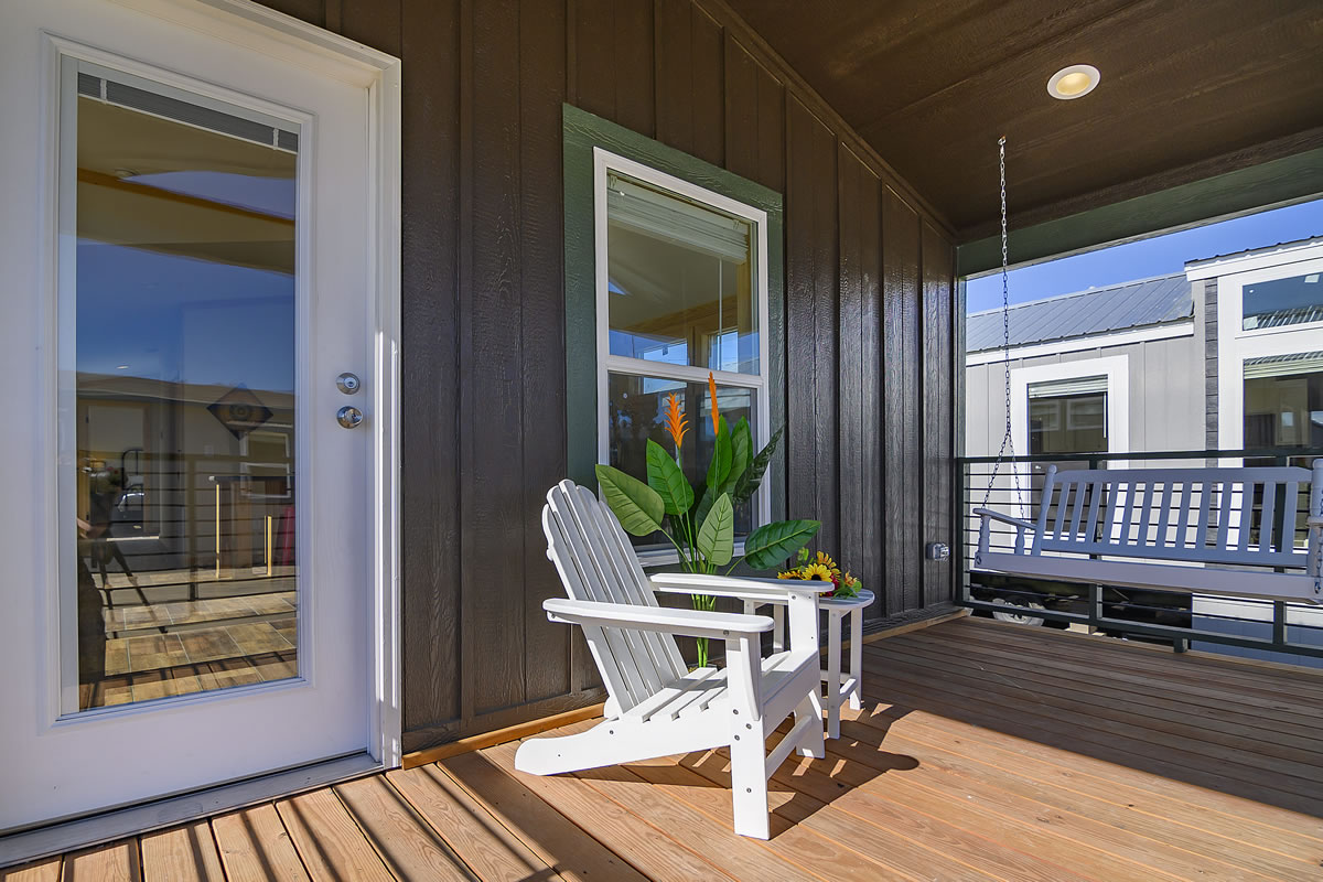 A cozy porch with a white Adirondack chair and potted plant on wooden decking, a swing in the background. Warm, inviting, and sunlit ambiance.