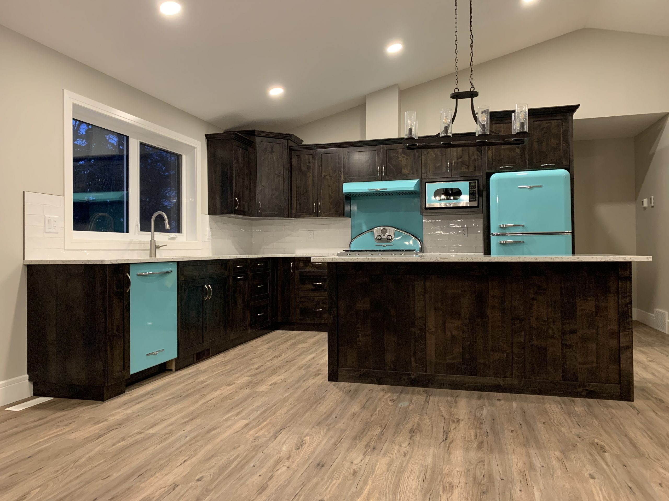 Modern kitchen with cool tones, featuring dark wood cabinets and retro-style turquoise appliances. Light hardwood floors and soft recessed lighting create a cozy ambiance.
