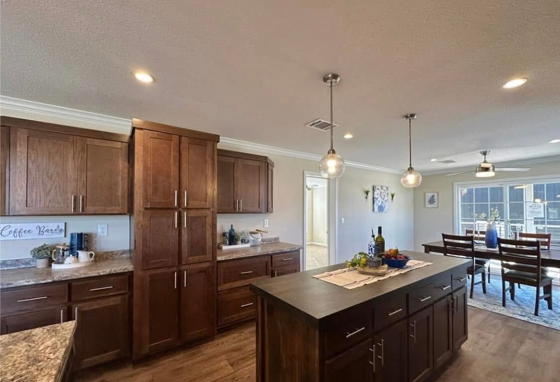 Modern kitchen with dark wood cabinets, marble countertops, and an island with pendant lights. Open dining area with natural light and wooden table.