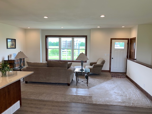 Spacious living room with large window showing greenery, two beige sofas, a small glass table, and soft lighting. Calm and inviting atmosphere.