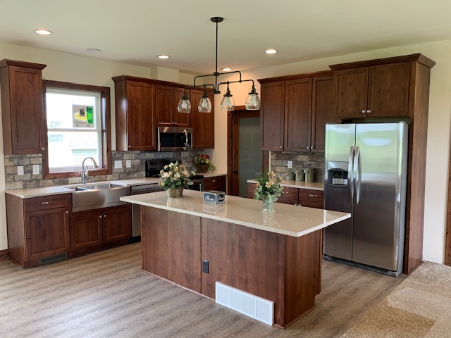 Modern kitchen with dark wood cabinets, stainless steel appliances, and a central island featuring pendant lights. Bright and inviting atmosphere.