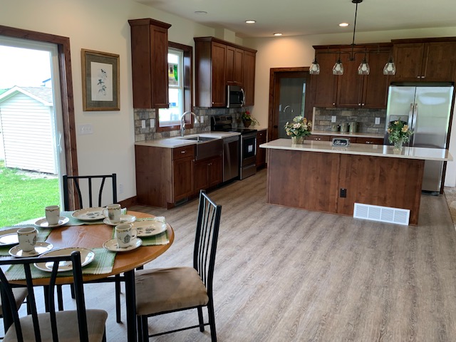 A spacious kitchen with wooden cabinets, stainless steel appliances, and a central island. A round dining table with four chairs is set by a window, offering a cozy, inviting feel.