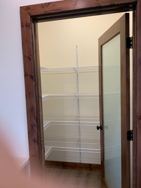 An empty pantry with white wire shelves, a wooden frame, and a frosted glass door. The shelving offers ample storage space in a neutral-toned room.