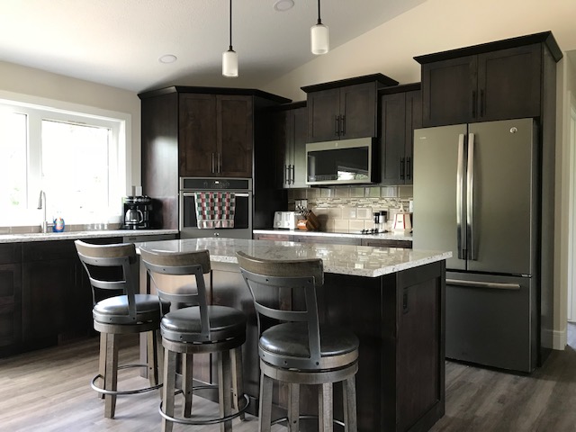 Modern kitchen with dark wood cabinets, stainless steel appliances, and a gray countertop island with three stools. Bright, airy, and inviting.