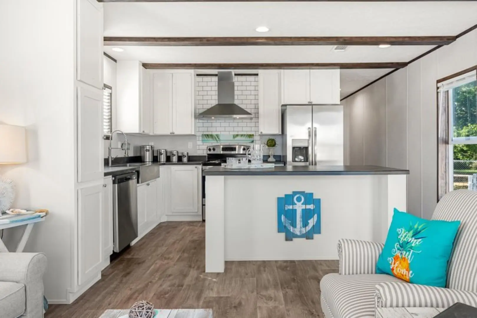 Modern kitchen and living area with white cabinets, stainless steel appliances, and a cozy seating area. Nautical decor adds a serene, inviting touch.