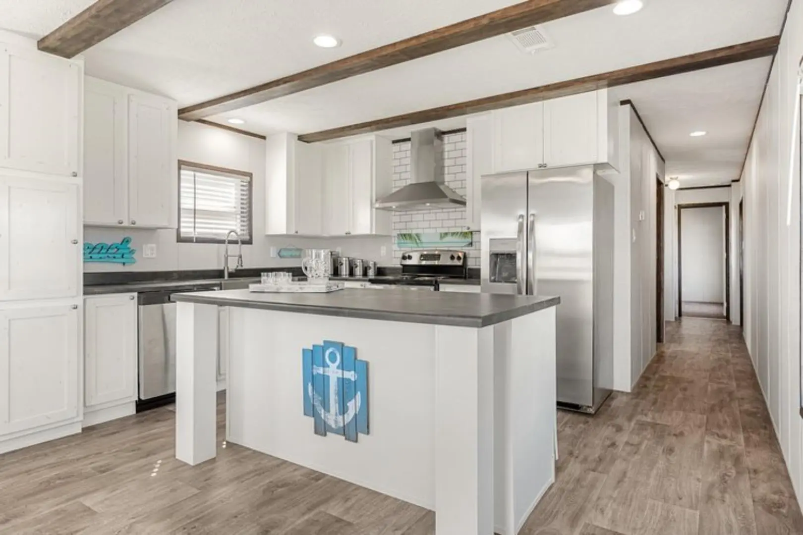 Modern kitchen with a nautical theme features white cabinets, stainless steel appliances, and an island with anchor decor. Wooden beams add warmth.