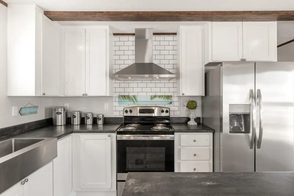 Bright, modern kitchen with white cabinets, stainless steel fridge, and stove. Subway tile backsplash, metal range hood, and black countertops.