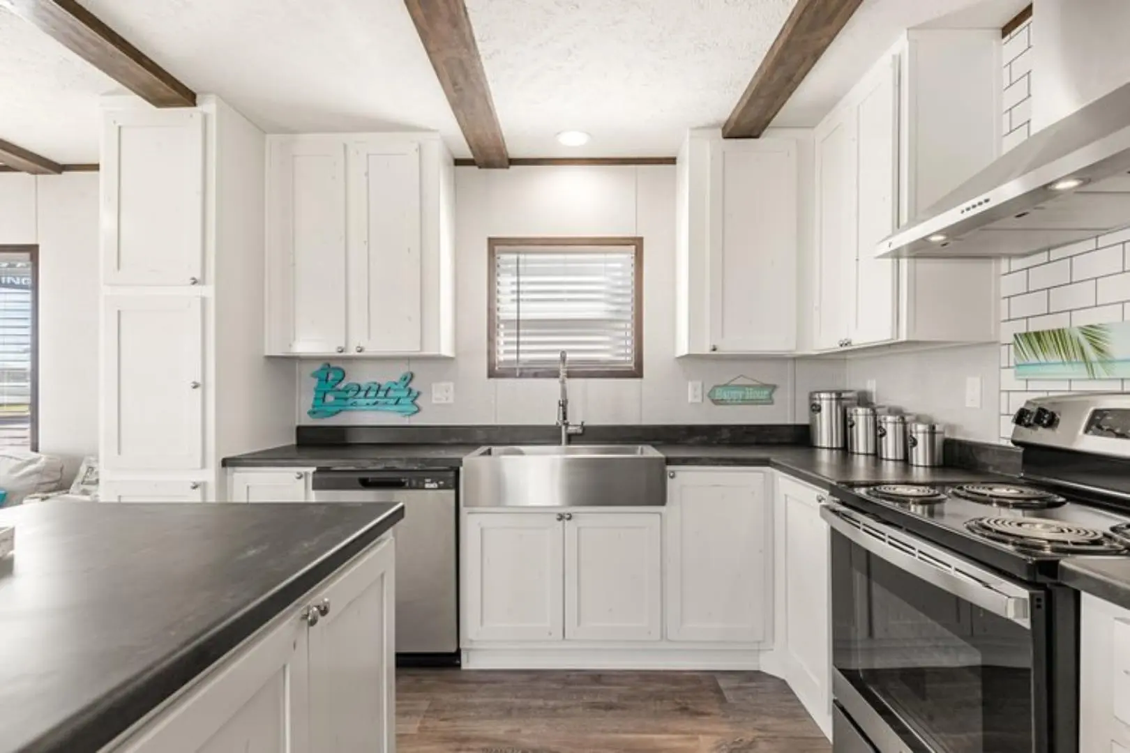 Modern kitchen with white cabinets, dark countertops, stainless steel appliances, and a farmhouse sink. Sunlight filters through a window with blinds. Cozy ambiance.
