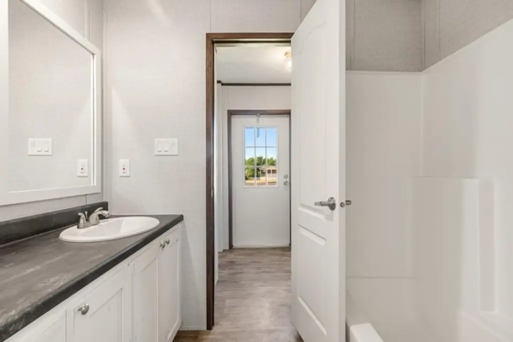 Bright bathroom with a white tub, open door, and a view of the hallway. Modern sink on a dark countertop; peaceful and minimal décor.