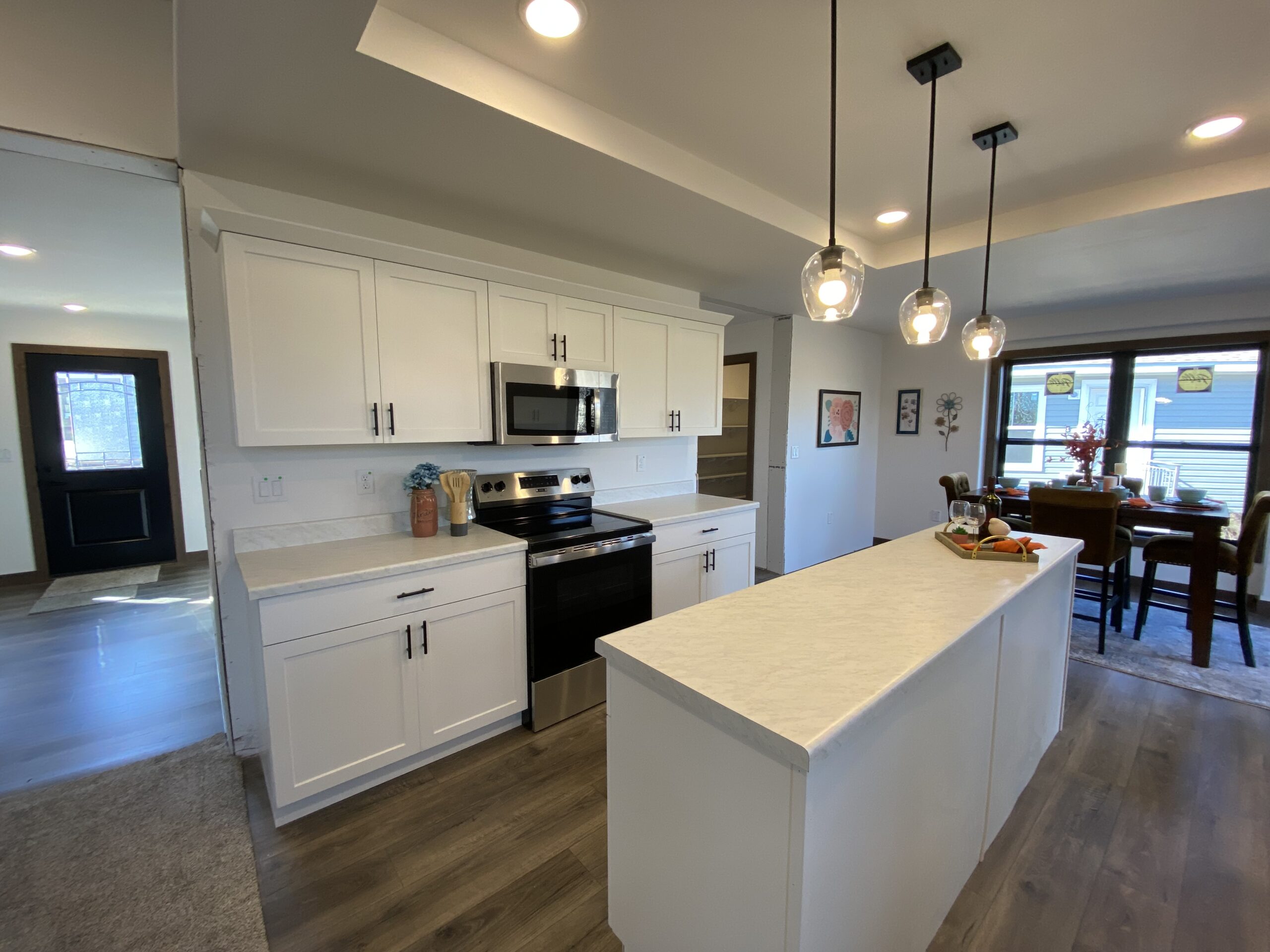 Modern kitchen with white cabinets, stainless steel appliances, and a central island lit by pendant lights. Dining area with a table in the background.