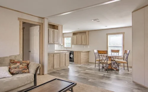 A cozy, modern open-plan living space with light wood flooring. Features a sofa, coffee table, wooden dining set, and a kitchen with natural light.
