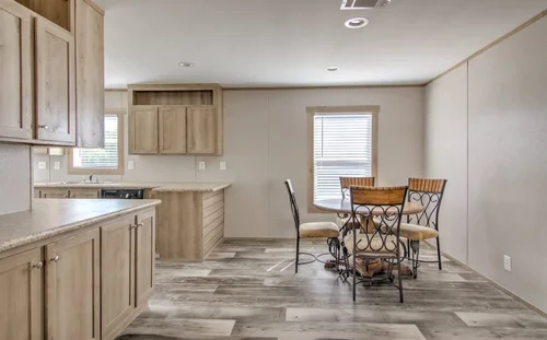 Cozy, modern kitchen with light wood cabinetry, gray flooring, and a round black table with wicker chairs by a window. Bright, minimalist, inviting space.