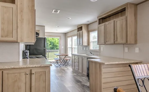 A bright, spacious kitchen features light wood cabinets and countertops. Large windows illuminate the space, with a small table and chairs by the window.
