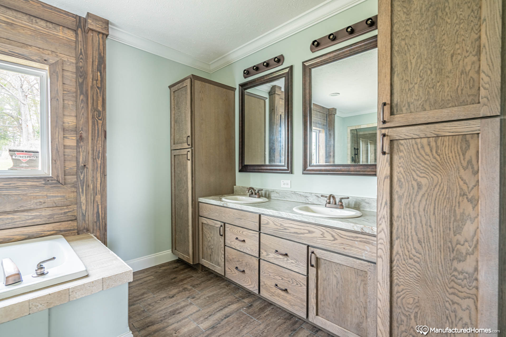 A modern bathroom with rustic wood accents features two sinks with marble countertops, large framed mirrors, a wooden cabinet, and a window by a bathtub.