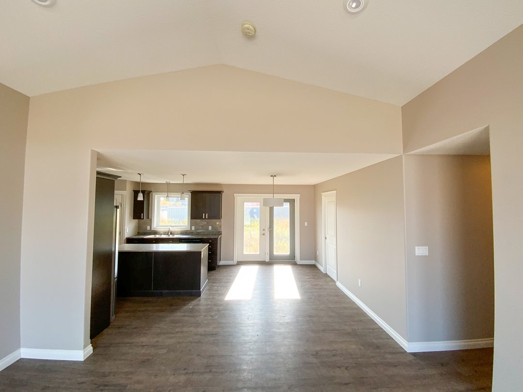 Spacious, sunlit room with high ceilings and muted beige walls. Features dark wood kitchen cabinets, pendant lights, and French doors to the outside.