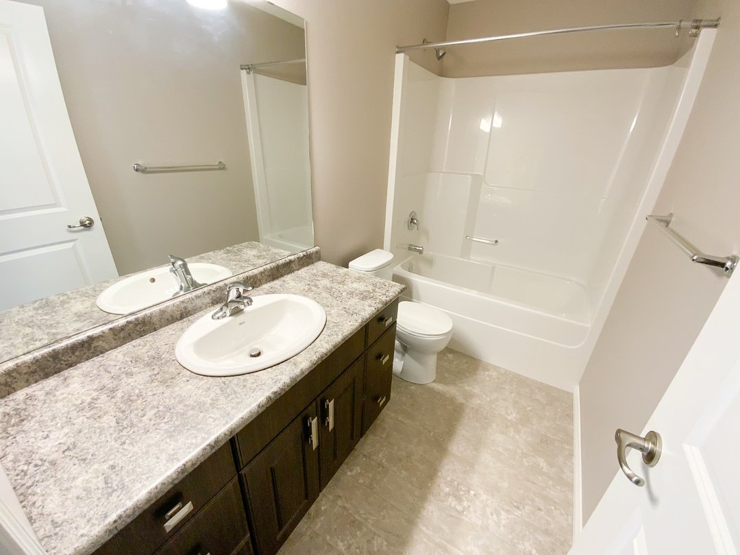 Modern bathroom with a marble countertop and dual sinks on a dark wood vanity. Features a white bathtub, beige walls, and a bright, clean ambiance.