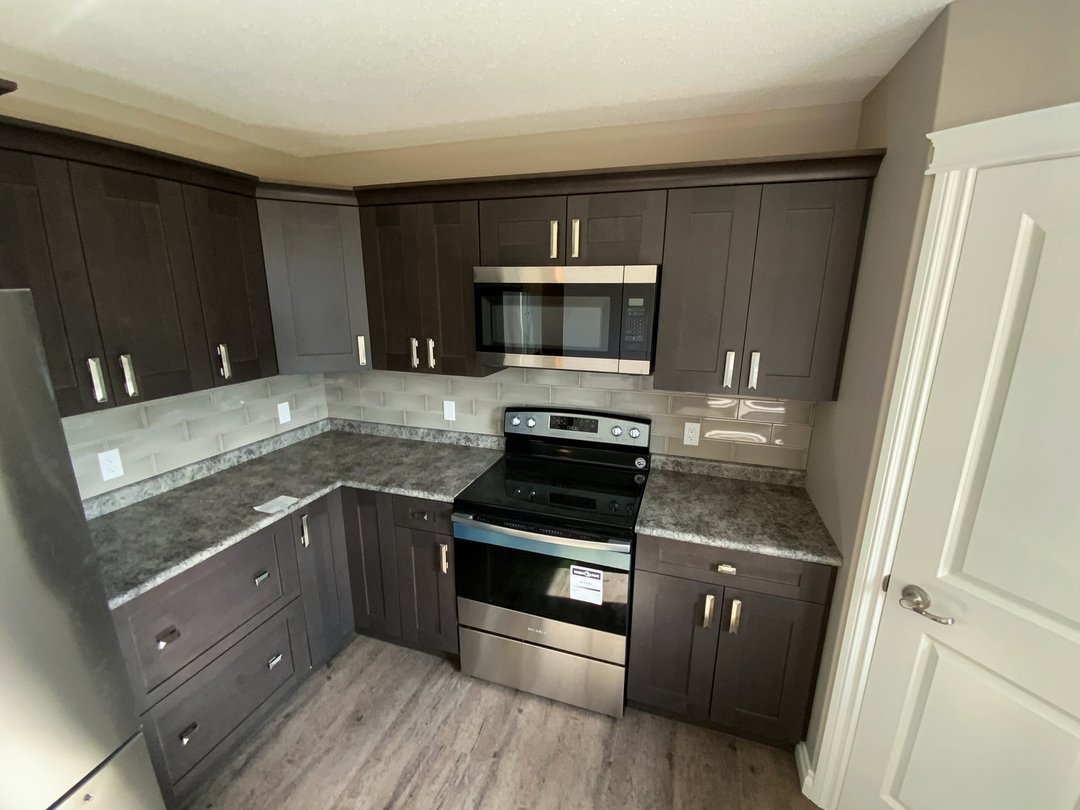 Modern kitchen corner with dark wood cabinets, granite countertops, stainless steel appliances, and light tiled backsplash. Clean and functional design.