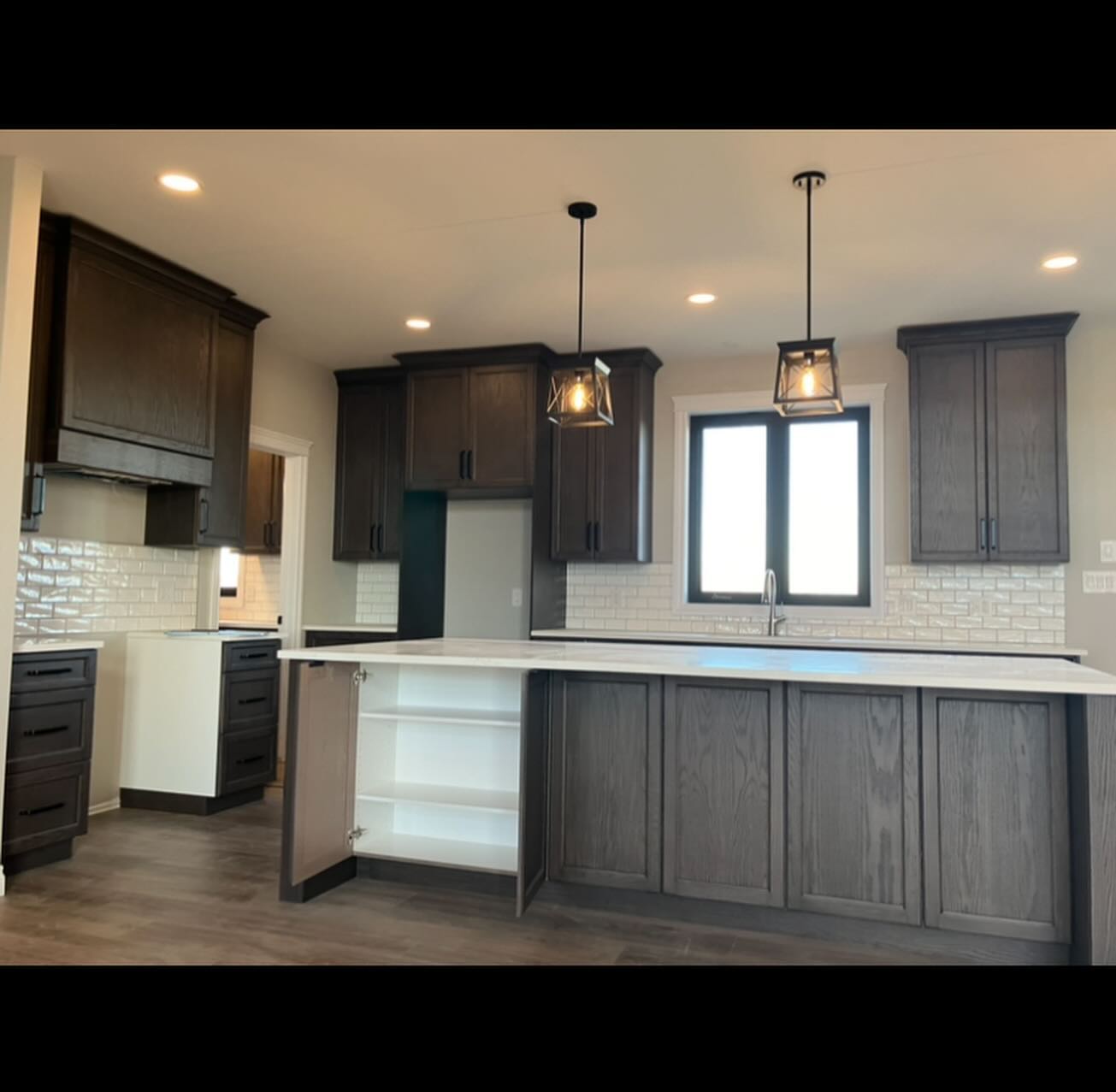 Modern kitchen with dark wood cabinets, white subway tile backsplash, and a large island with open shelving. Pendant lights hang above, creating a warm ambiance.