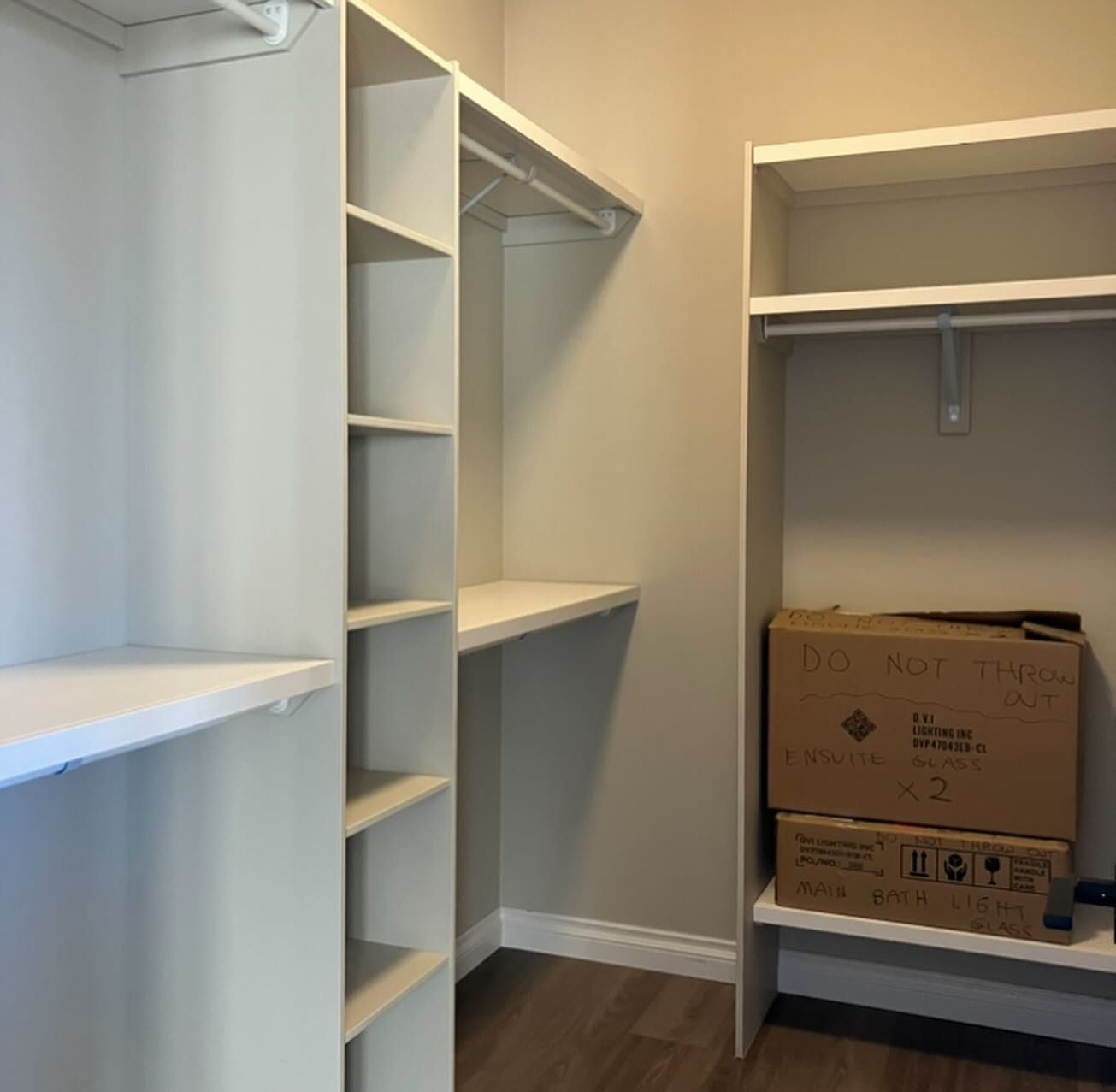 A spacious, empty white closet with built-in shelves and rods. Two cardboard boxes labeled "Do Not Throw Out" sit on a lower shelf, creating an organized yet stark atmosphere.