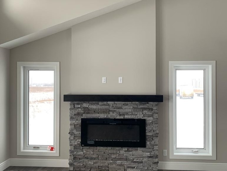 A modern living room features a stone fireplace with a black mantle, flanked by two vertical windows. The room is bright and minimalistic.