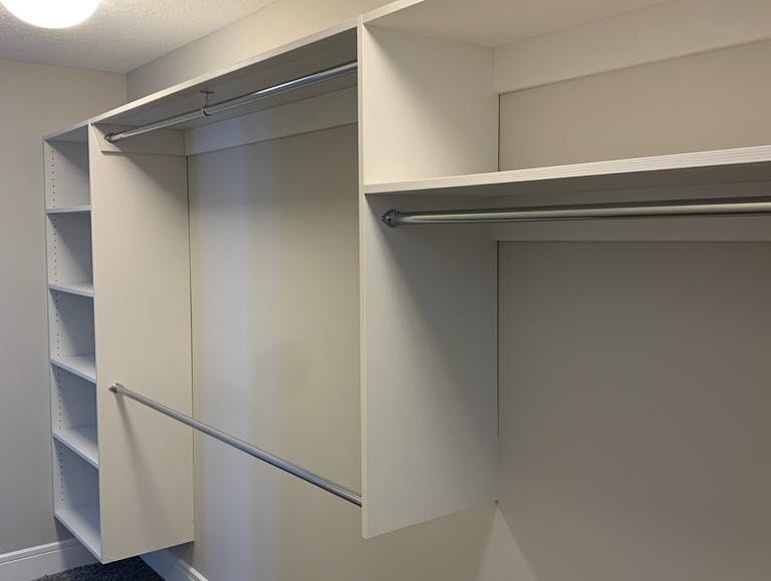 Empty walk-in closet with white walls and lighting. Features include multiple hanging rods and open shelves on the left. The space feels clean and modern.