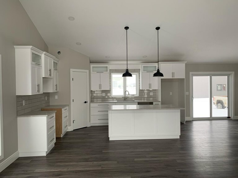 Modern kitchen with white cabinets, gray tile backsplash, and dark wood floors. Features an island with pendent lights and a window and sliding door.