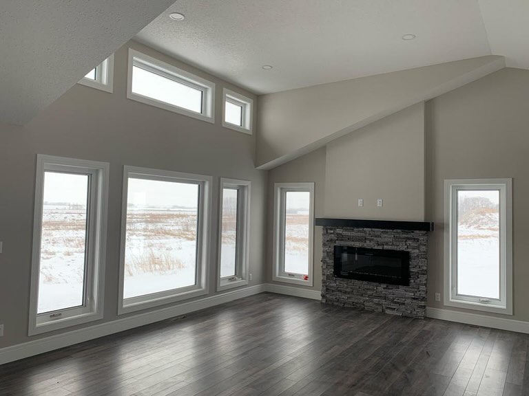 Spacious room with large, snow-view windows, high ceiling, dark wood floor, and stone fireplace. Modern, airy ambiance with natural light.