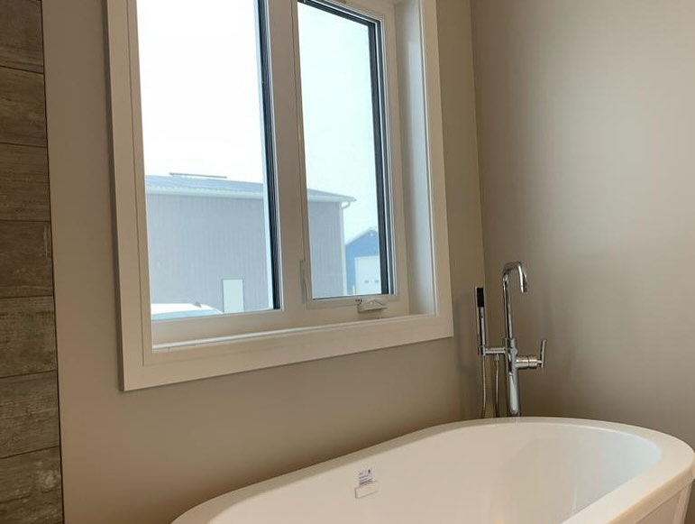 Modern bathroom with a white oval bathtub, chrome faucet, and a large window offering natural light. Neutral walls create a calming atmosphere.