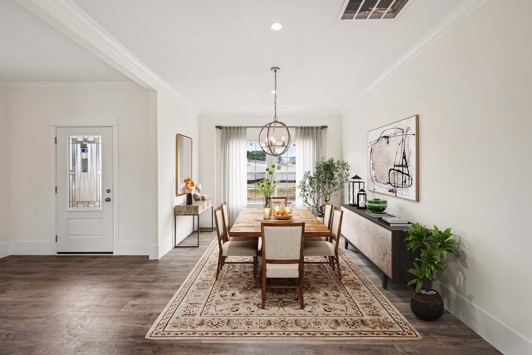 Elegant dining room with a wooden table, beige cushioned chairs, and a patterned rug. Pendant light above, abstract art and plants create a welcoming tone.