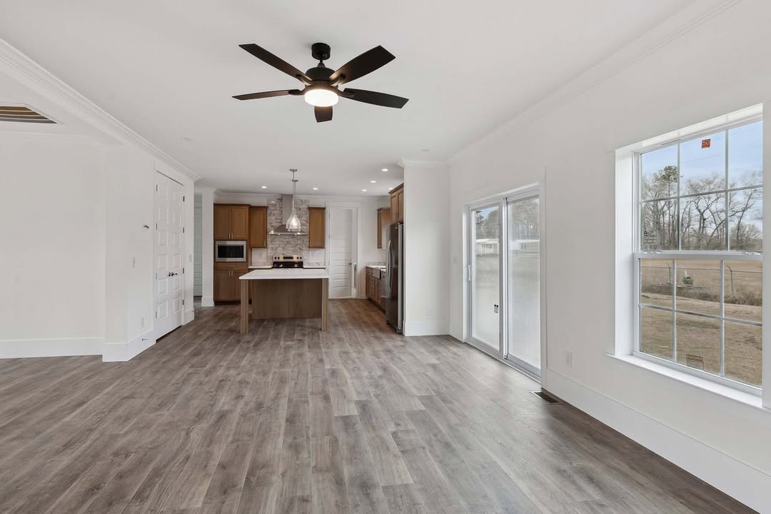Modern kitchen with wood flooring, island, and stainless steel appliances. Bright space with ceiling fan and large windows overlooking a yard.