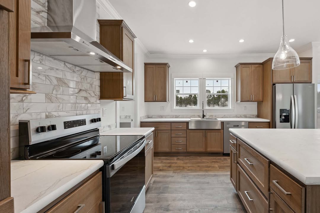 Modern kitchen featuring wooden cabinets, white countertops, stainless steel appliances, and a central island under pendant lighting. Bright and spacious.