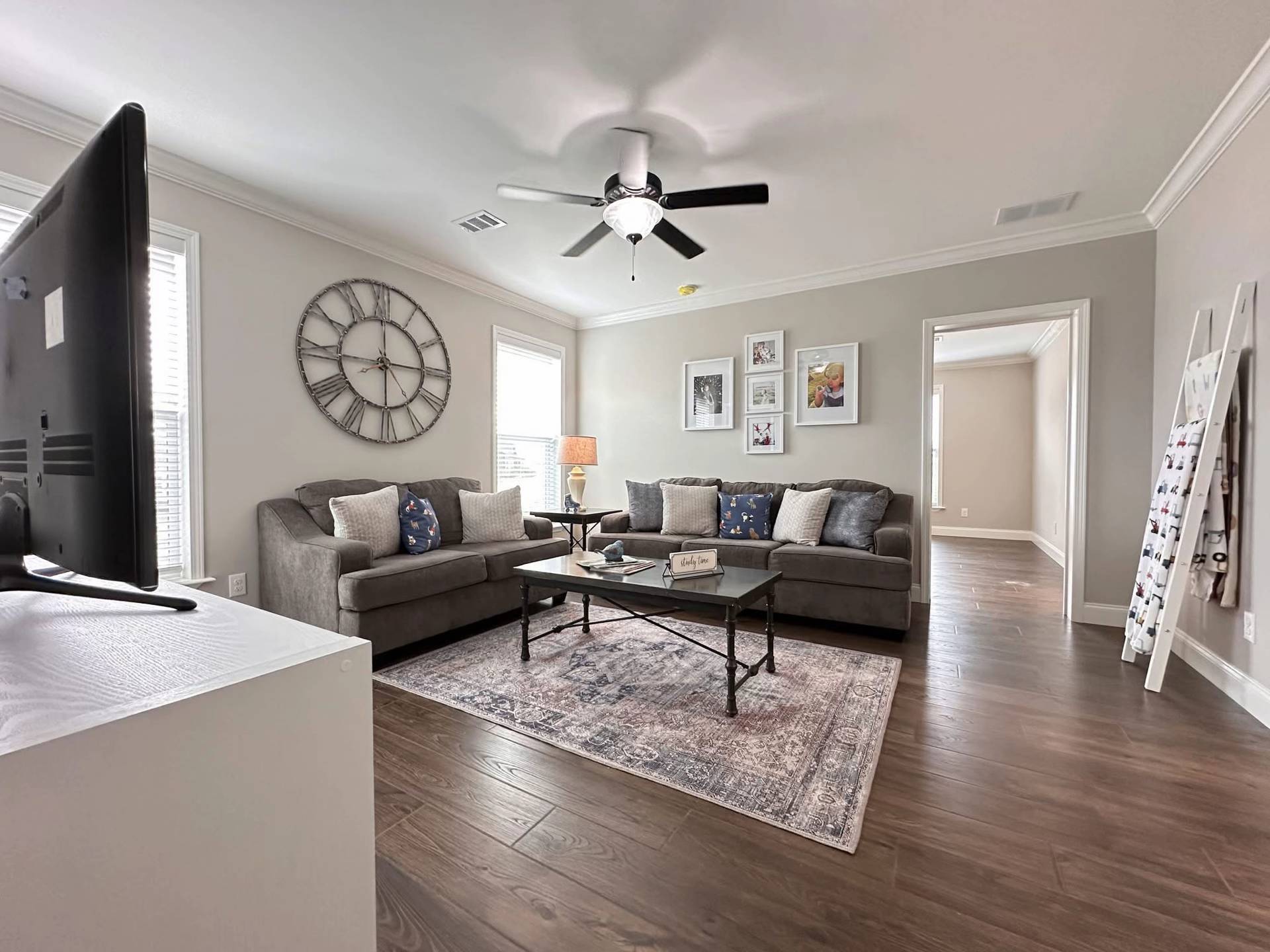 Modern living room with gray walls, two gray sofas, and a glass coffee table on a patterned rug. A large wall clock and framed art add elegance.