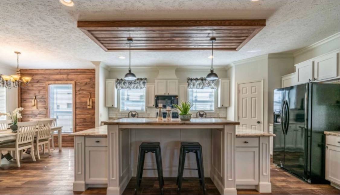 Spacious kitchen with a central island, white cabinets, pendant lights, black stools, and wooden accents. Adjacent dining area features a rustic wooden wall.