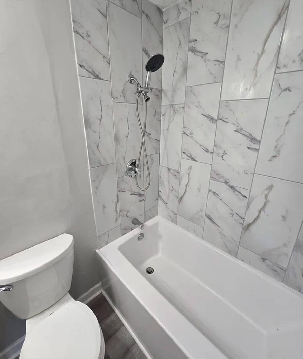 Compact, modern bathroom with a white toilet and sink vanity, accented by a silver mirror and towel ring, set against gray walls and wood floor.