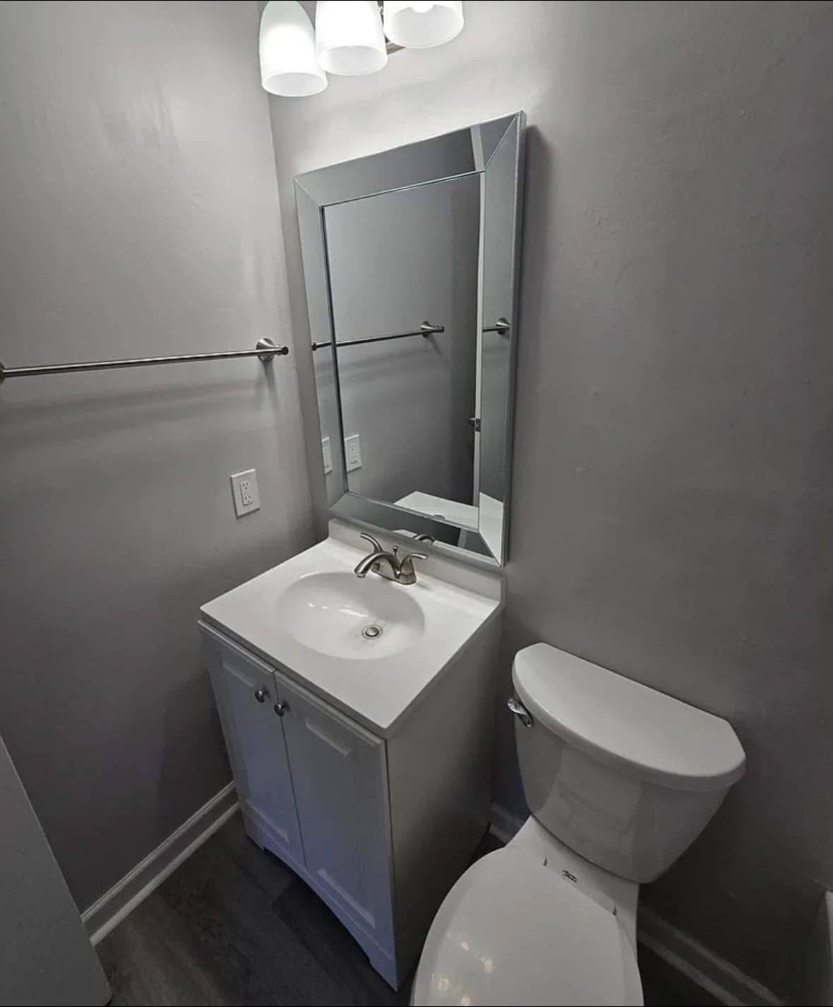 Small bathroom with a wall-mounted mirror reflecting a countertop sink and faucet. Next to it is a toilet. The space is compact and minimally decorated.