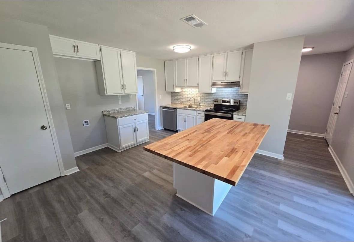 Modern kitchen with light gray walls, wooden flooring, white cabinets, steel appliances, and a central wooden island. Bright, clean, and inviting atmosphere.