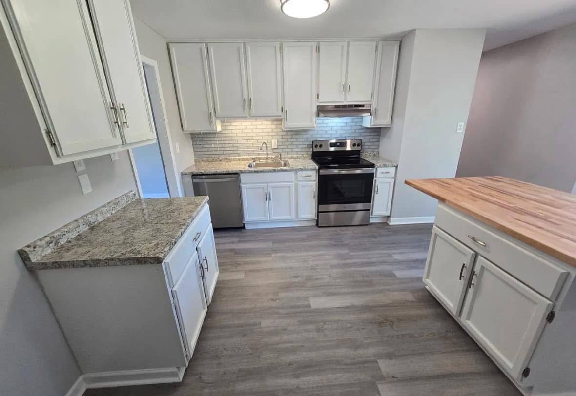 Modern kitchen with white cabinets, gray countertops, and stainless steel appliances. Light wood flooring and a central island create an open and inviting space.