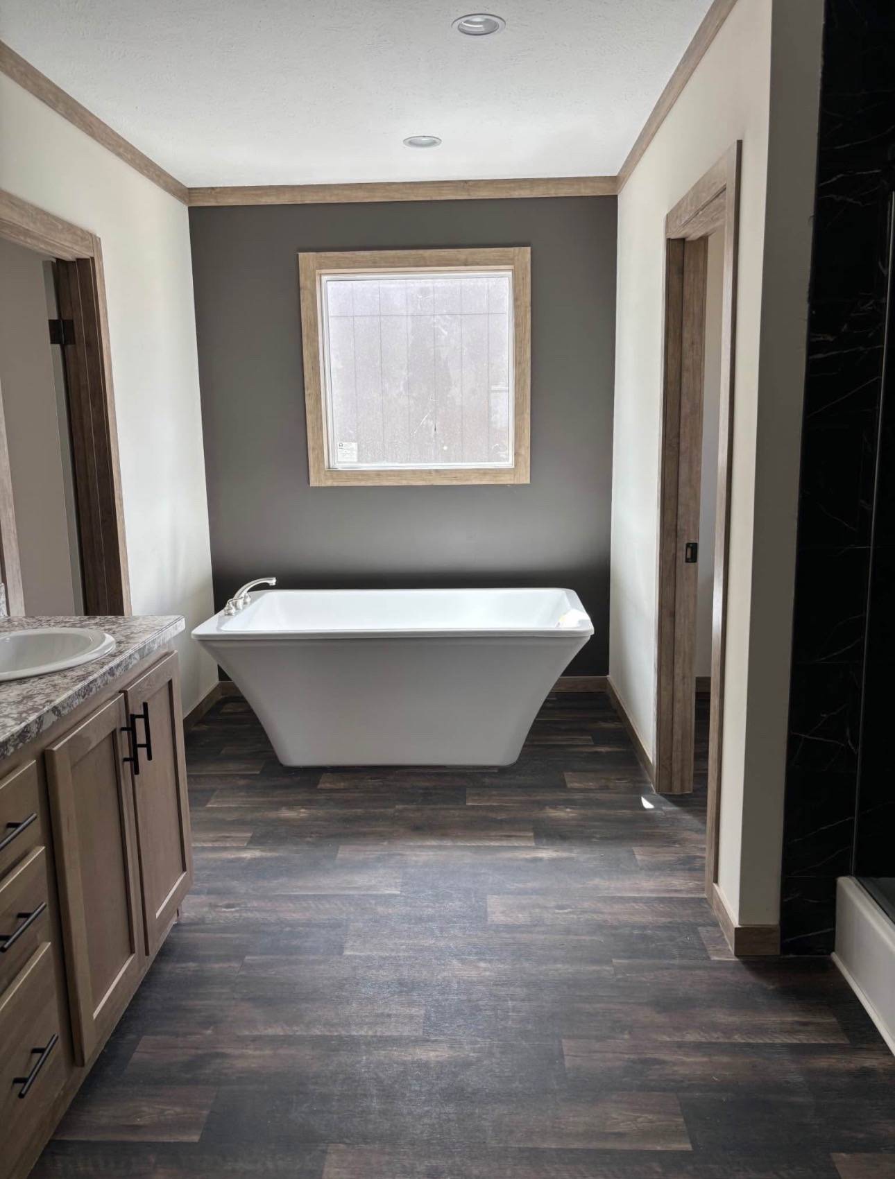 Modern bathroom with dark wood flooring, featuring a sleek white freestanding tub under a frosted window. The neutral tones add a calm, minimalist feel.
