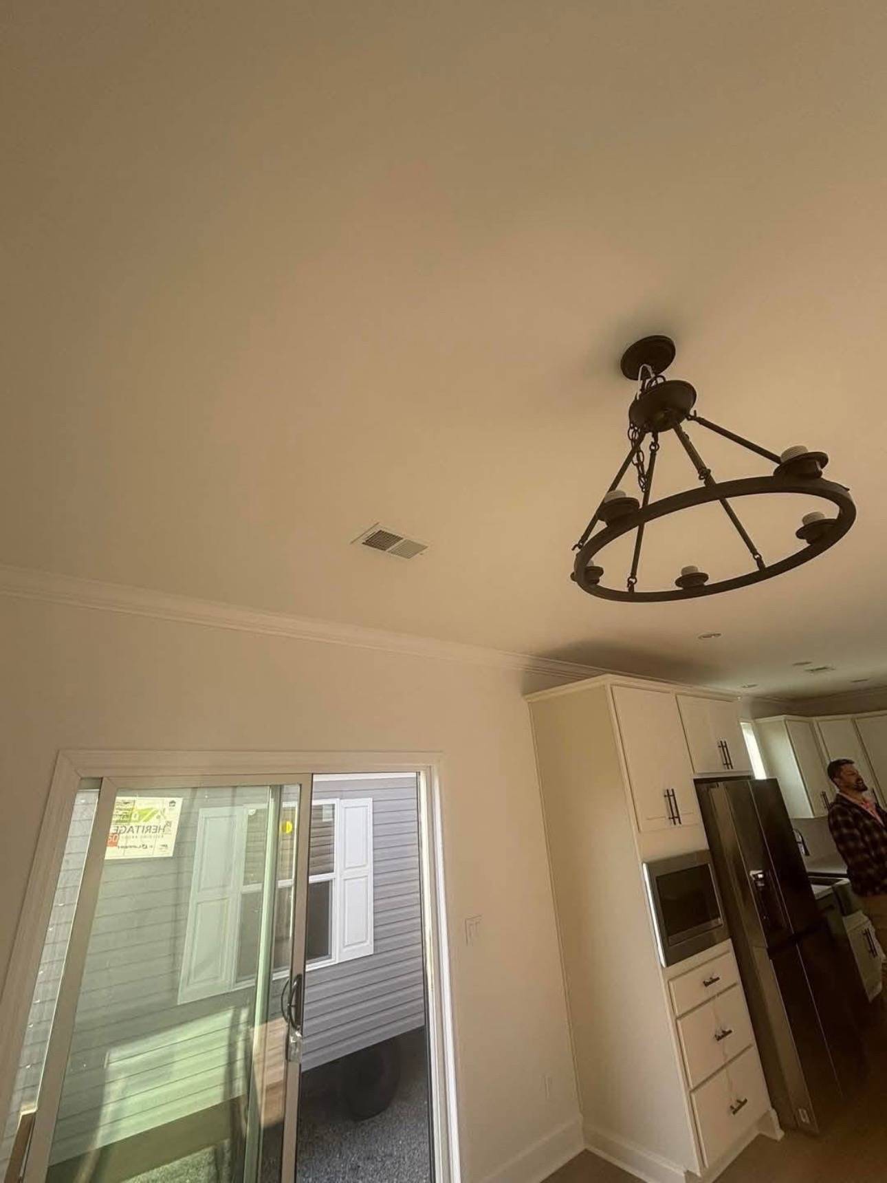 Modern kitchen interior with a rustic light fixture on the ceiling. Features white cabinets, stainless steel appliances, and a glass sliding door, creating an open, airy feel.