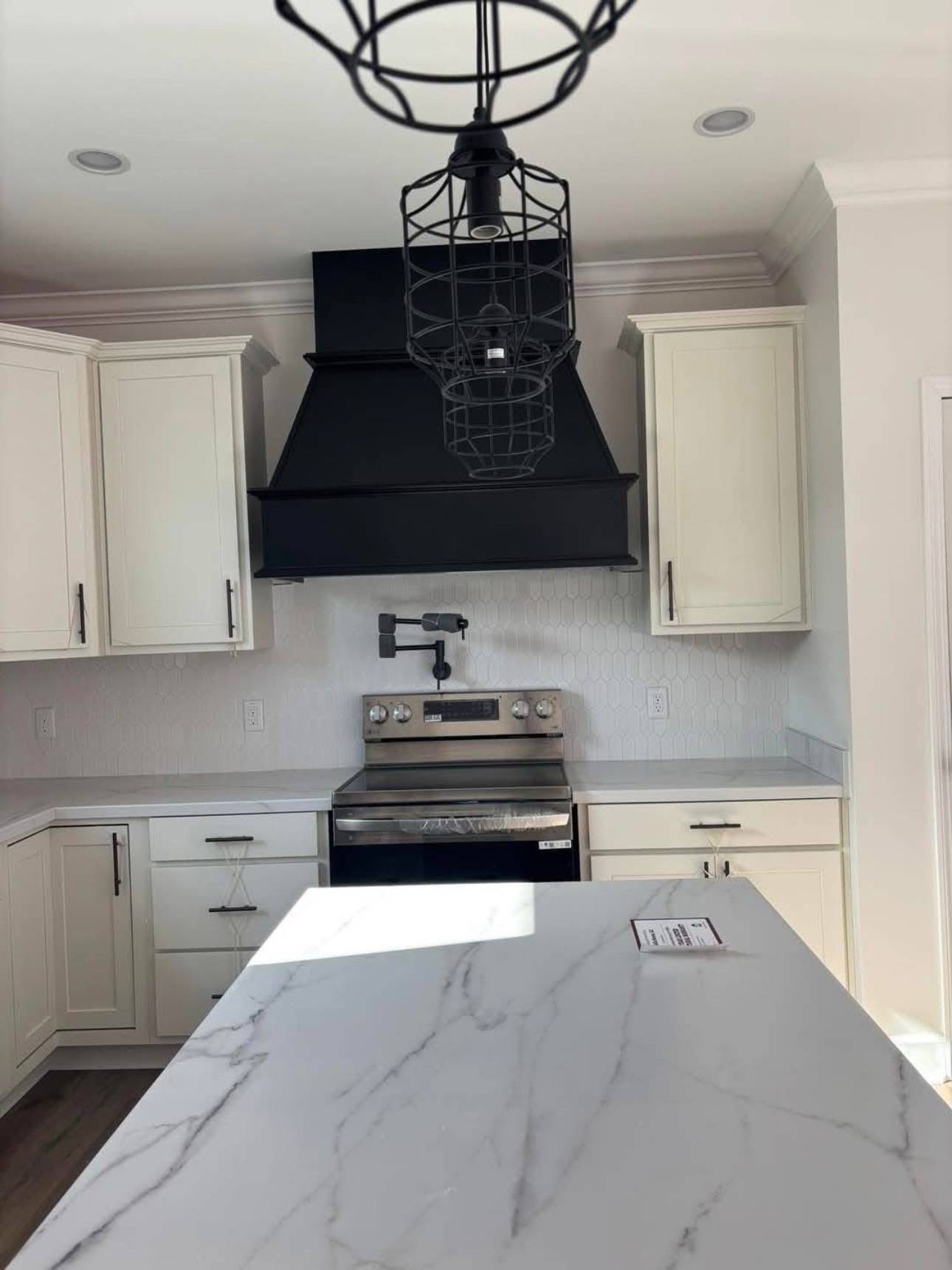 Modern kitchen with white cabinets, a stainless steel stove, and black range hood. A marble island countertop and geometric pendant light add elegance.