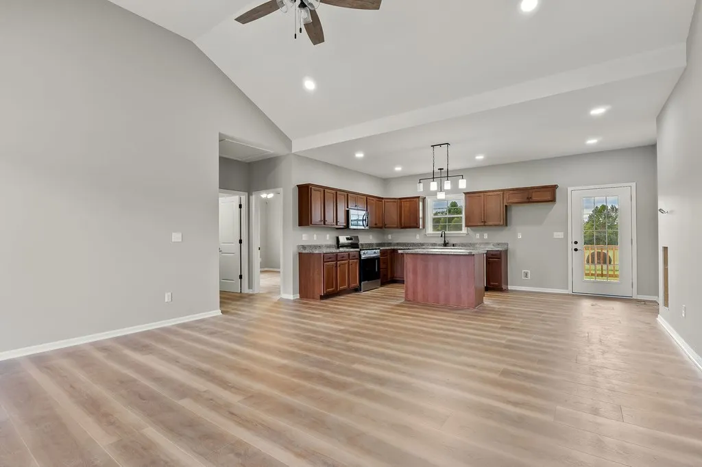 Spacious modern kitchen with light wood floors, dark wood cabinets, and a central island. Large windows and glass door for natural light. Airy and inviting ambiance.
