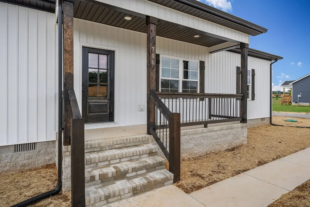 Cozy white house with a rustic porch featuring dark wood pillars and railing. Steps lead to a black door. Fresh sod surrounds the new build.