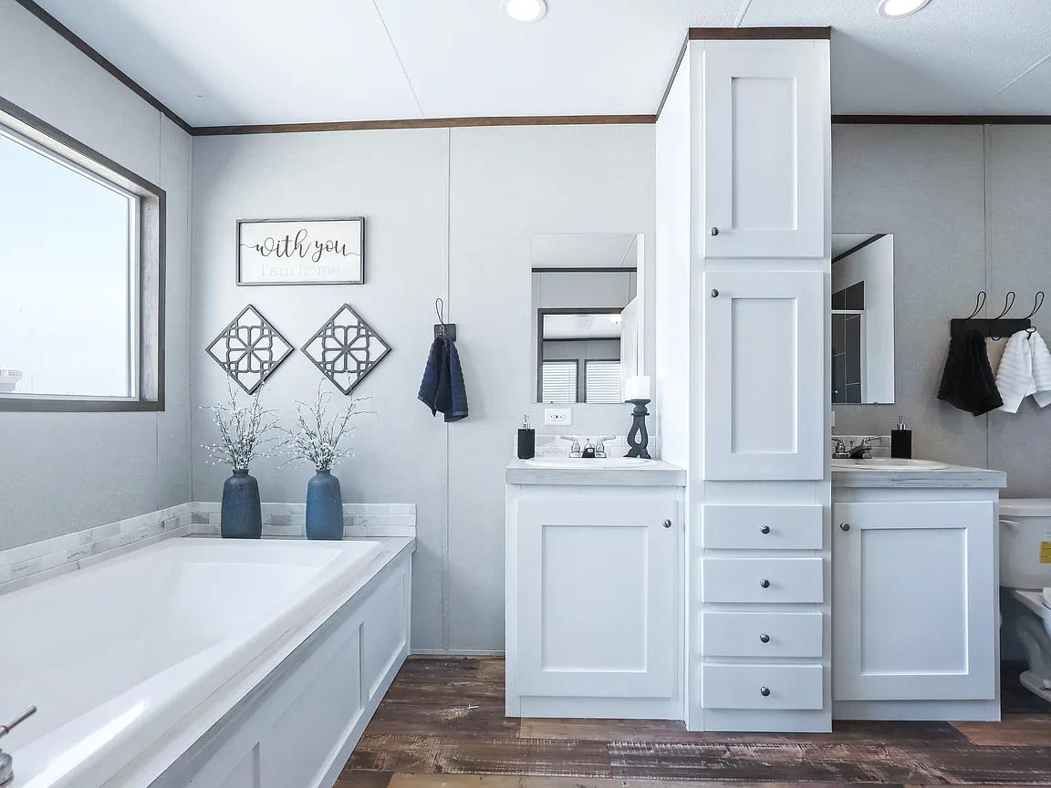 A bright, modern bathroom with white cabinets, a large bathtub, and decorative wall art. The space feels clean and inviting, with a calming atmosphere.