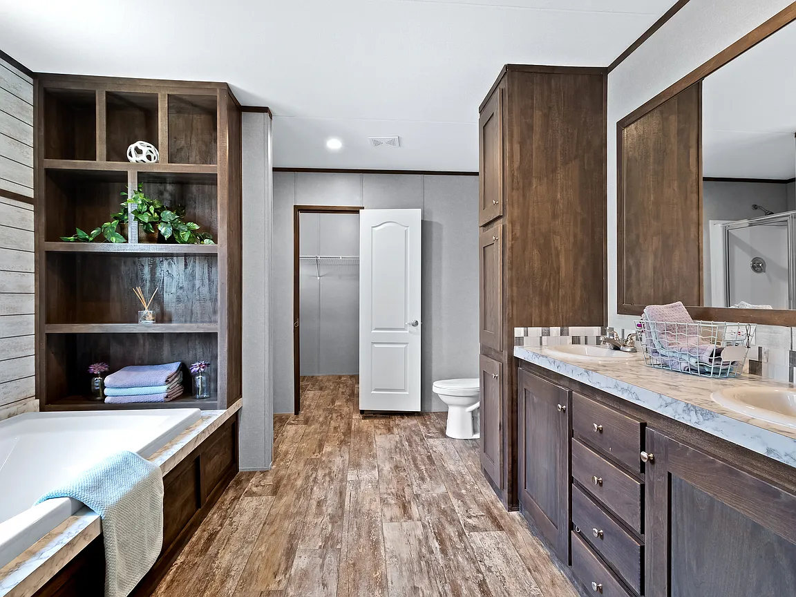 Spacious modern bathroom with rustic wood cabinetry, bathtub with a towel, large mirror, and open closet. The ambiance is warm and inviting.