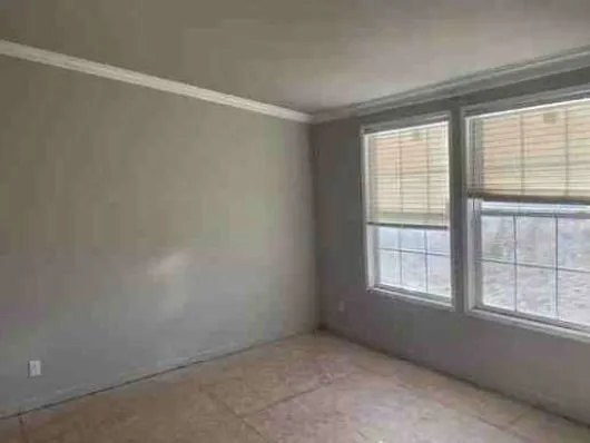 A rural landscape featuring a ranch-style house with a curved gravel driveway, surrounded by dry grass and a wide sky with scattered clouds, evokes a serene and isolated atmosphere.