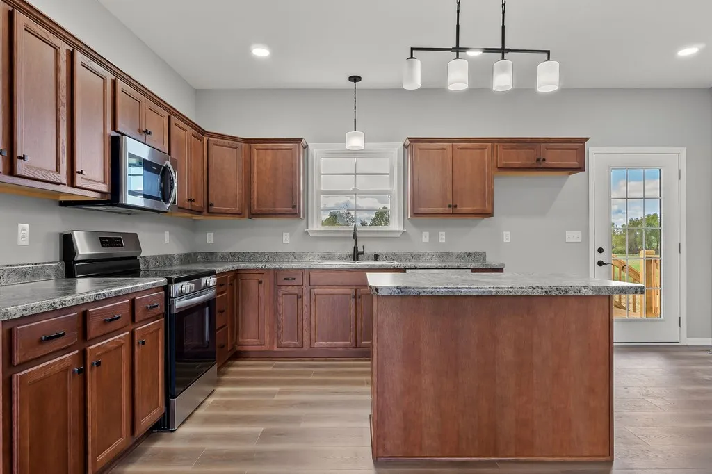 Spacious kitchen with cherry wood cabinets, granite countertops, and stainless steel appliances. Modern pendant lighting and a door lead to an outdoor deck.