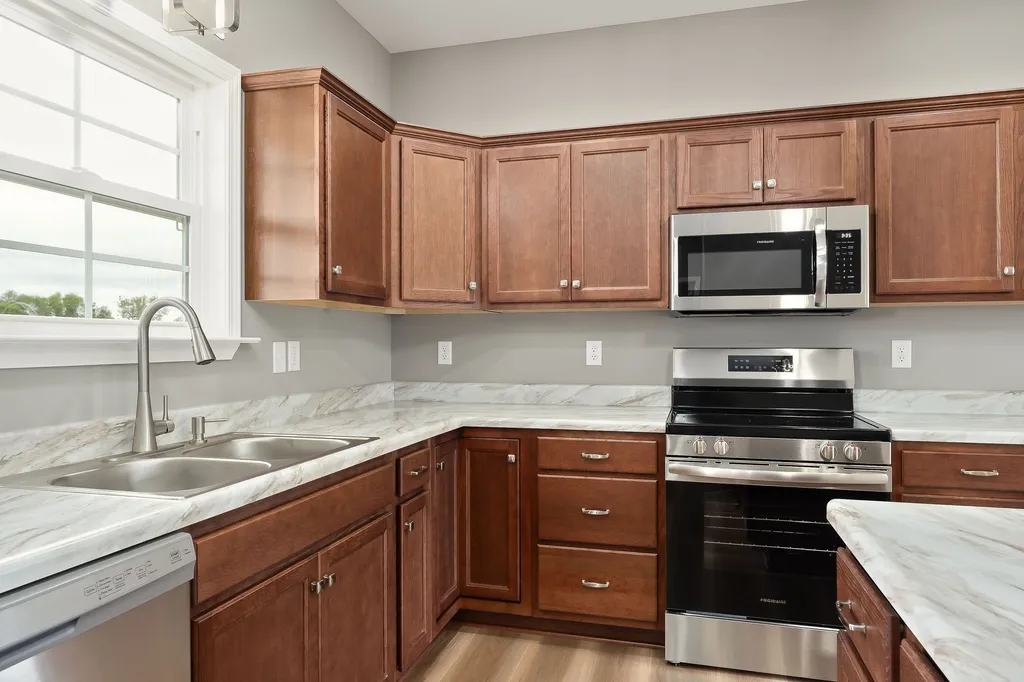 Spacious kitchen with wooden cabinets, marble countertops, stainless steel appliances, and a double sink by a window. Bright, clean, and modern.