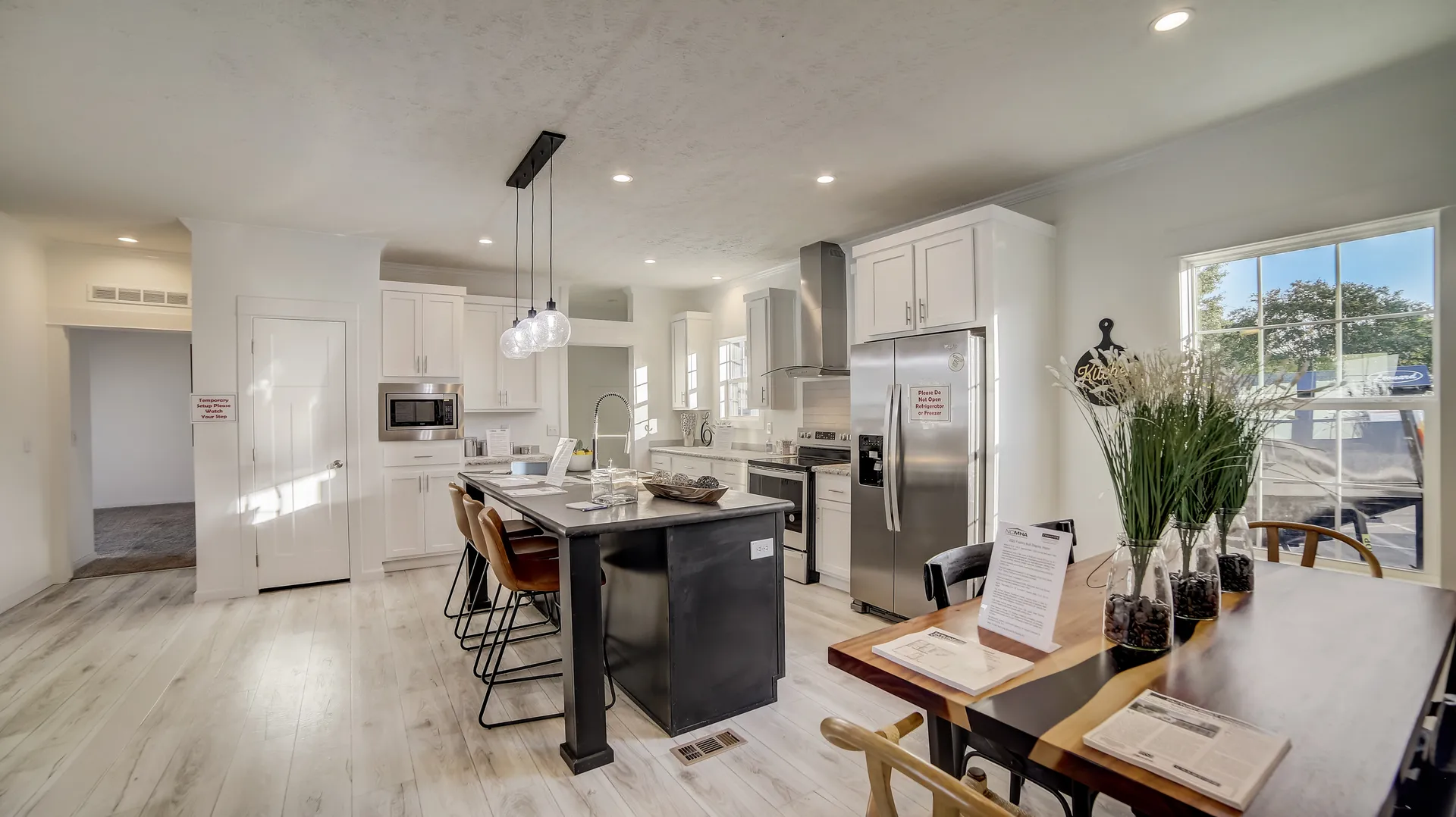 Bright, modern kitchen with white cabinets, stainless steel appliances, and a black island with brown stools. A dining table with flowers is nearby.